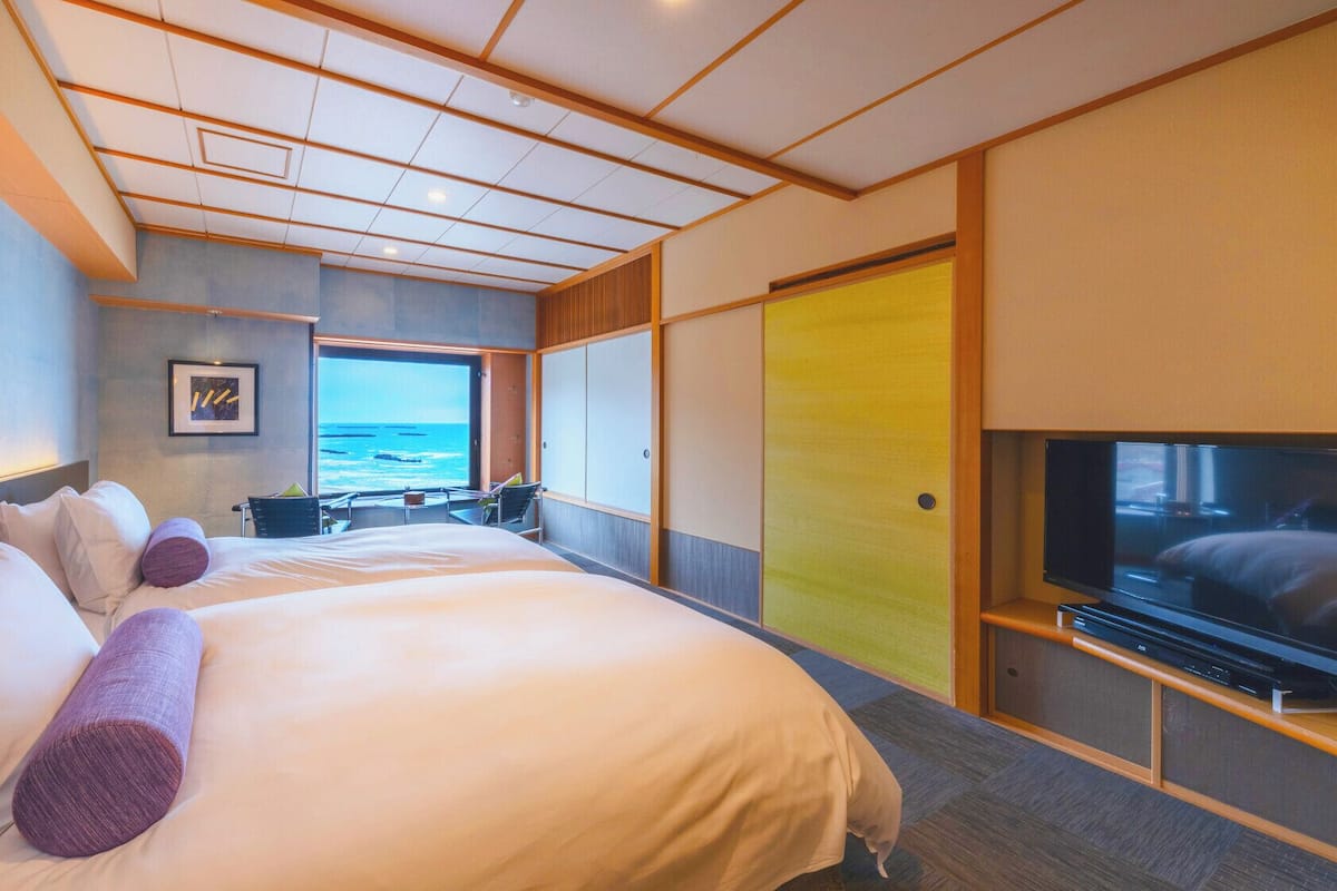 A hotel room with a large bed, a television, a view of the ocean, and a sliding door.