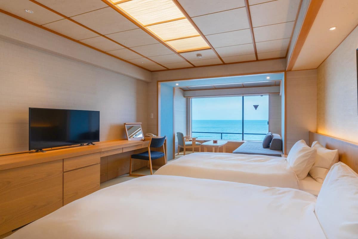 A hotel room with a TV, desk, and seating area with a view of the sea.