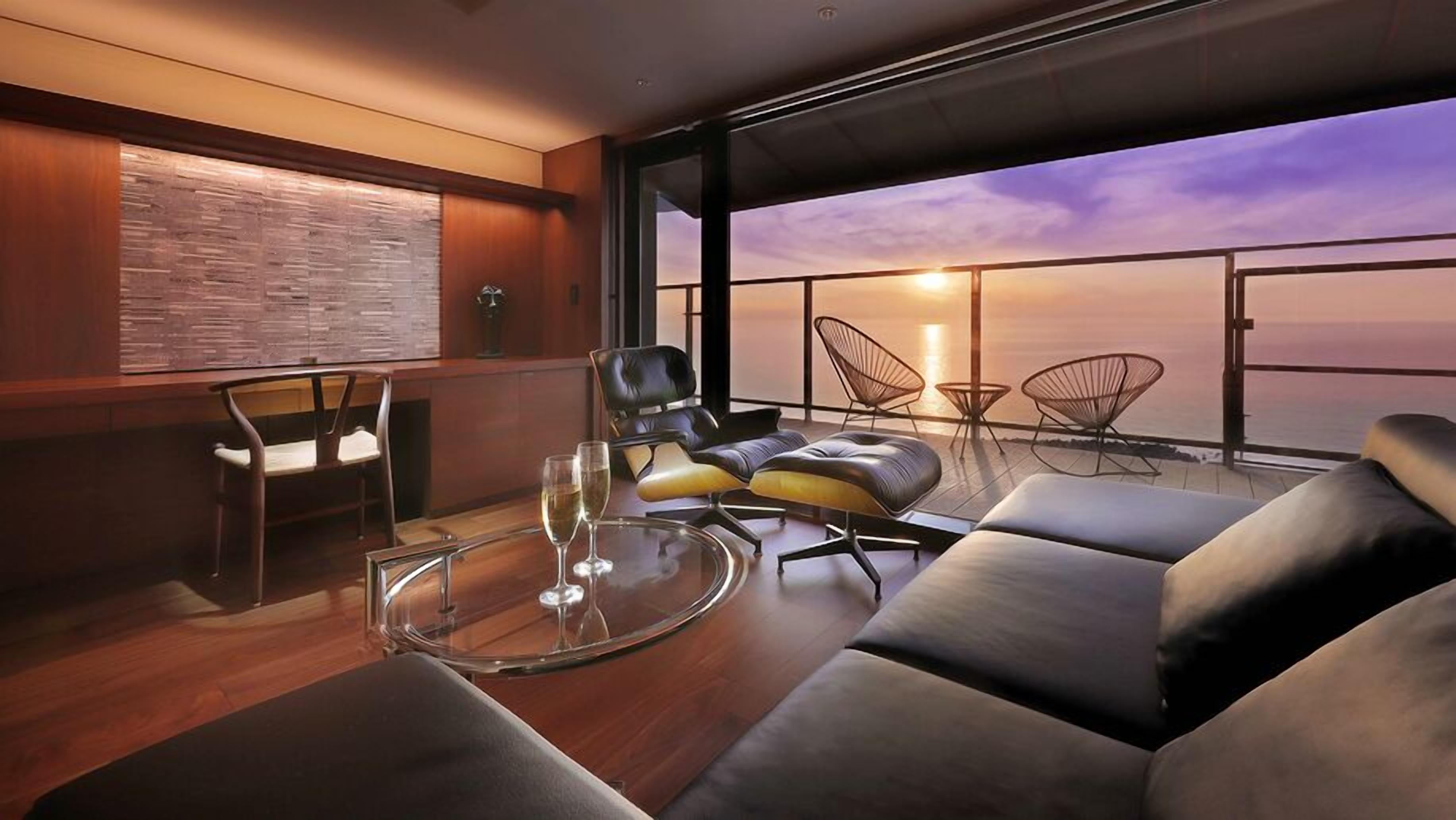 A modern interior with a glass table, leather seating, and a view of the sunset over the ocean.