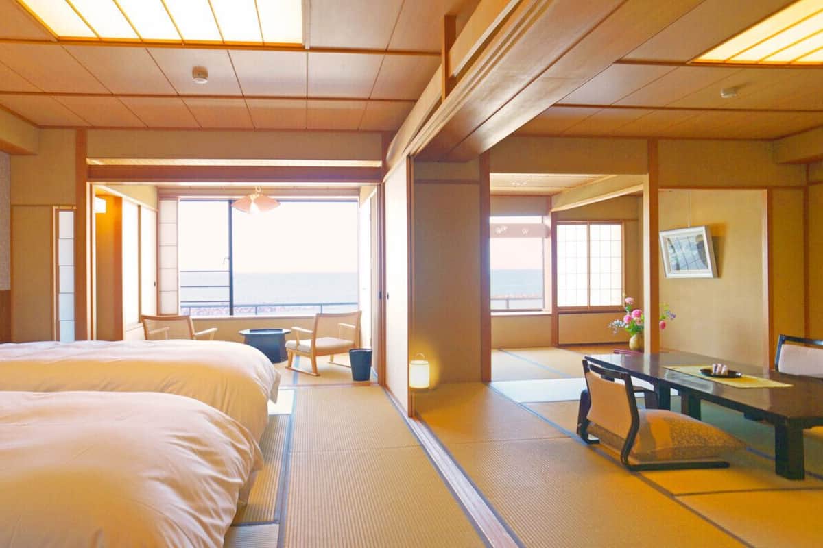 A hotel room with two beds, a desk, a chair, and a view of the sea.