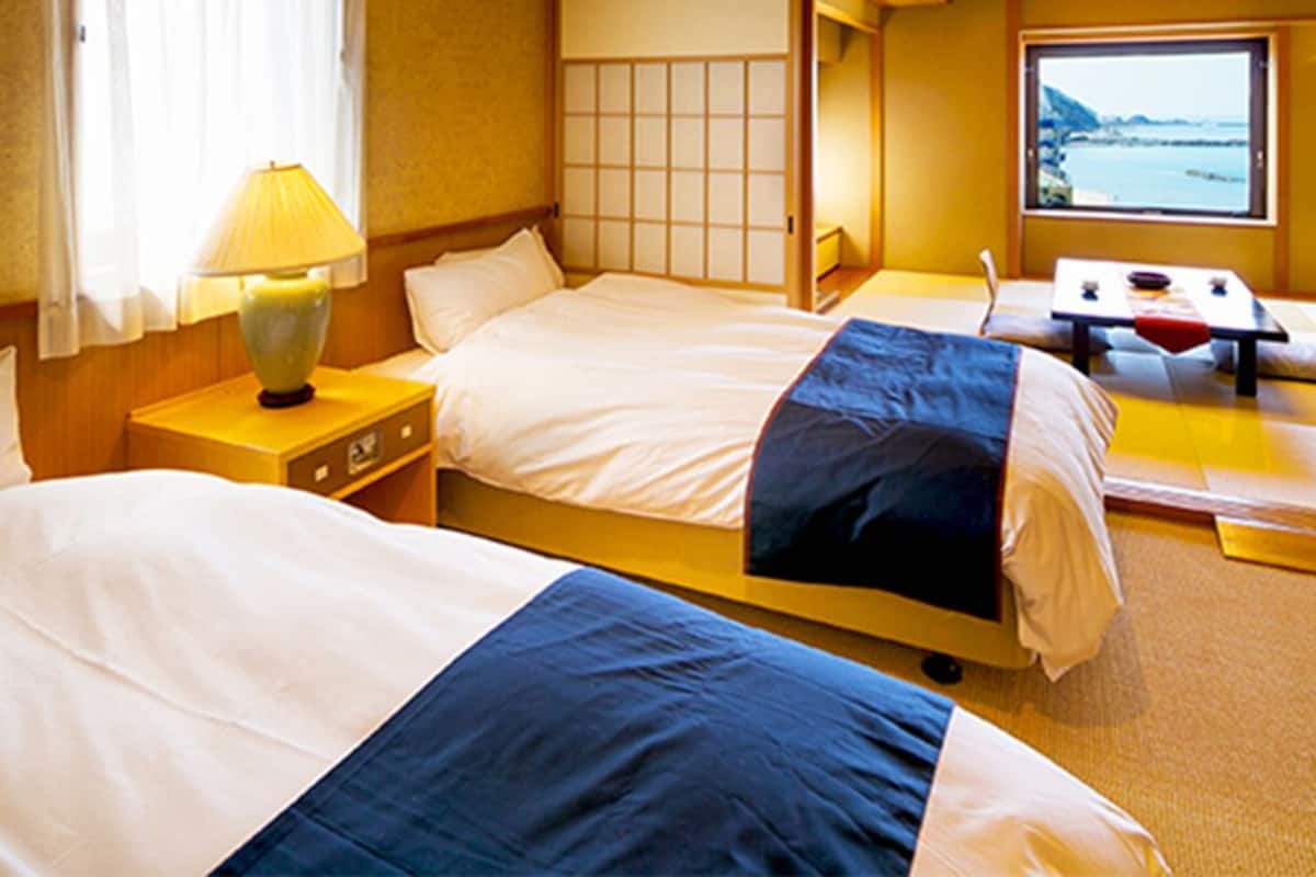 A hotel room with two beds, a table, and a view of the sea.