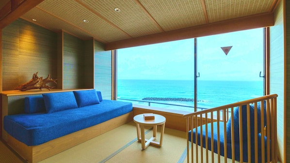 A room with a blue sofa, a small round table, and a view of the ocean. - Yusuitei Isagoya (Tsuruoka)