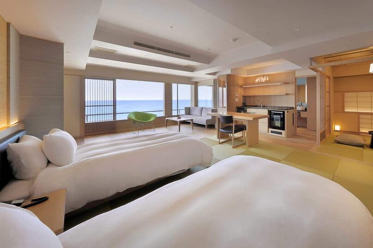 A hotel room with two beds, a dining area, a kitchen, and a view of the sea.