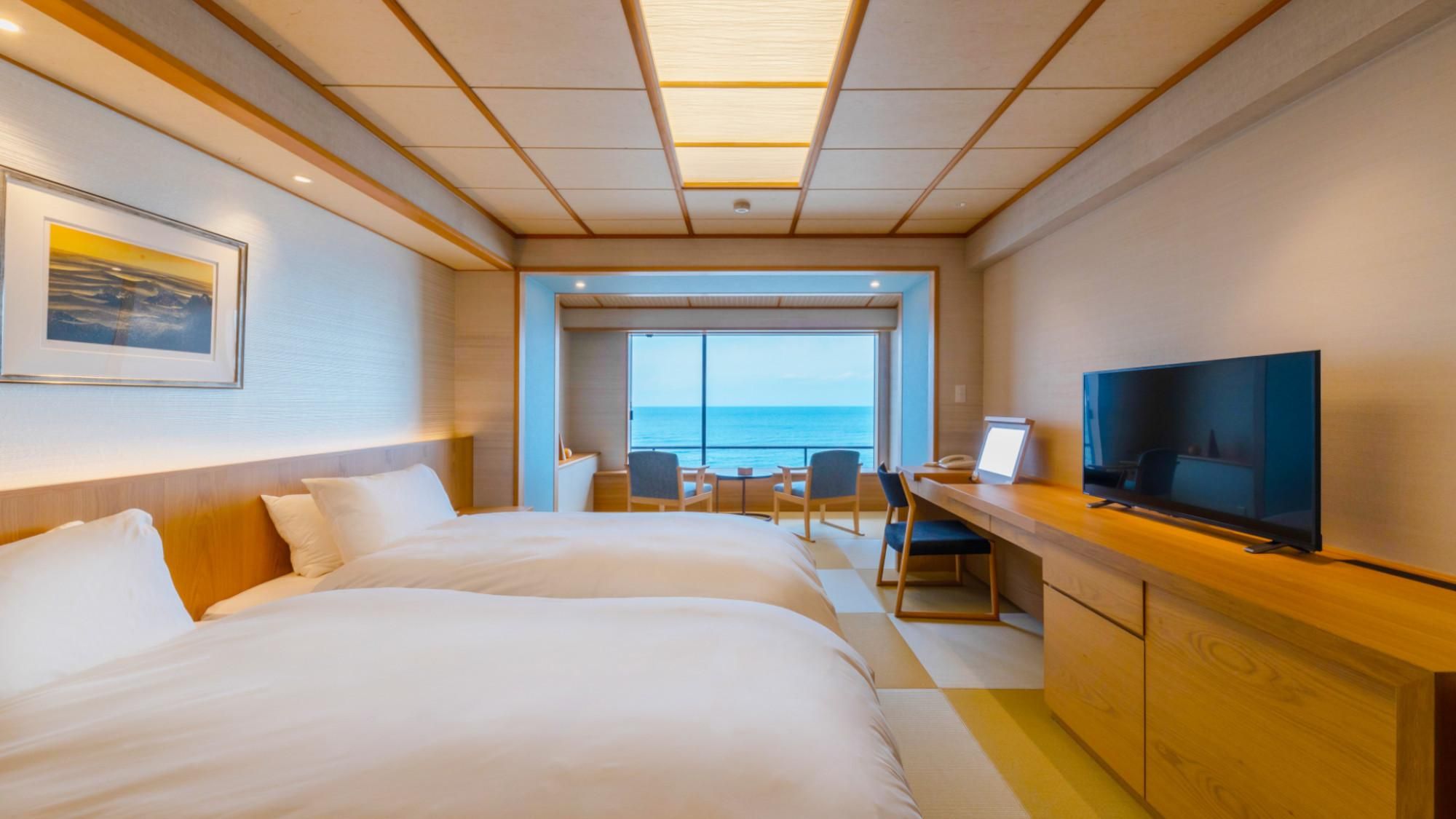 A hotel room with a bed, a desk with a television, and a view of the sea.