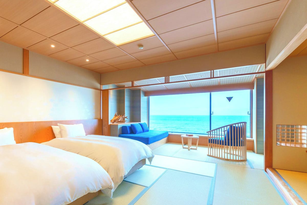 A room with a large bed, a seating area with a view of the sea, and a balcony with a railing.
