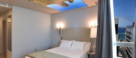 Habitación de hotel con cama, lámparas de noche, tragaluz en el techo y vistas de la ciudad a través de una ventana.