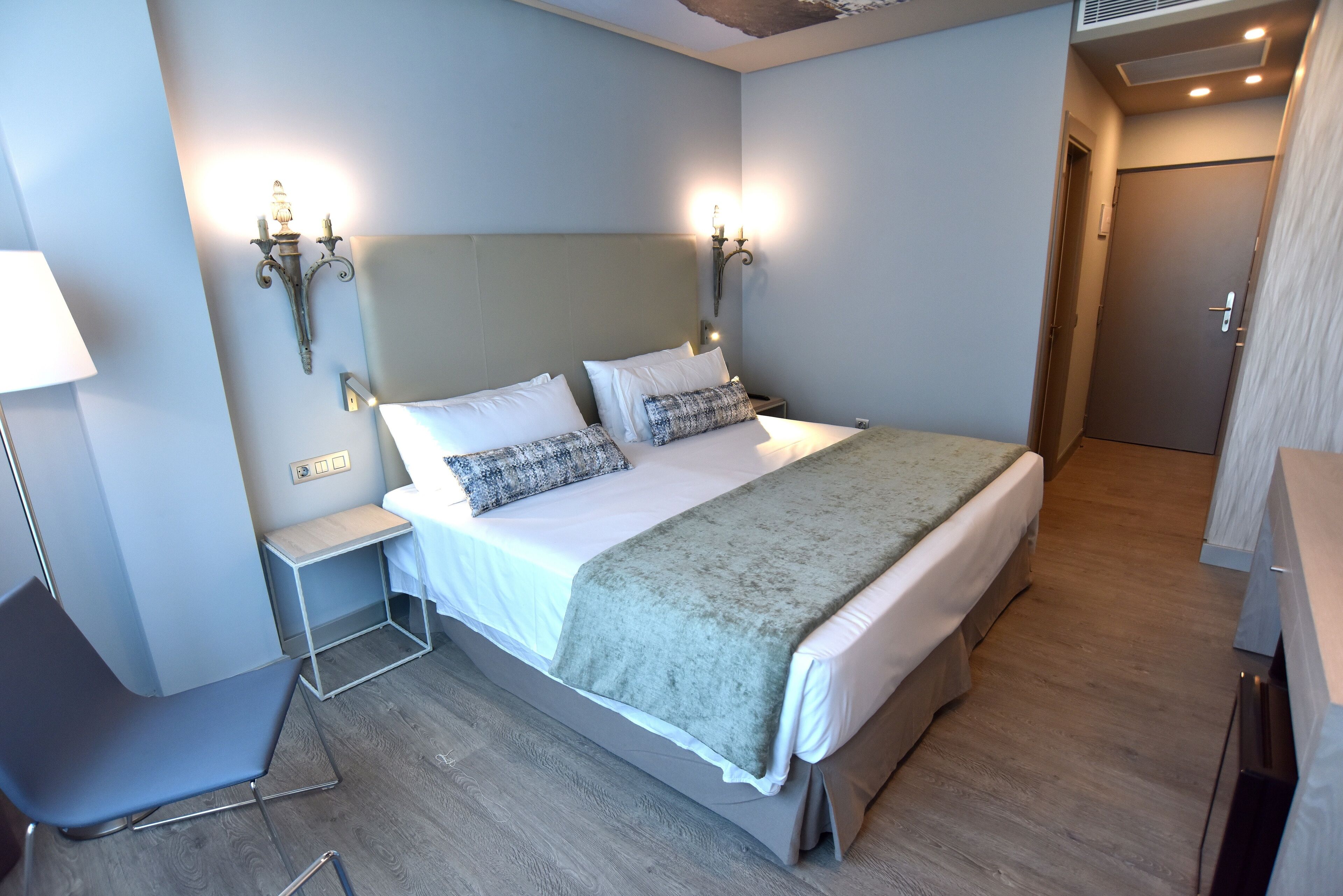 A modern hotel room with a large bed, bedside tables, a chair, and a wardrobe.