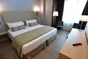 A hotel room with a large bed, a desk, a chair, and a remote control on the desk.