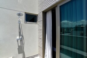 Un balcón con puerta de vidrio, una ventana pequeña y un rociador de ducha.
