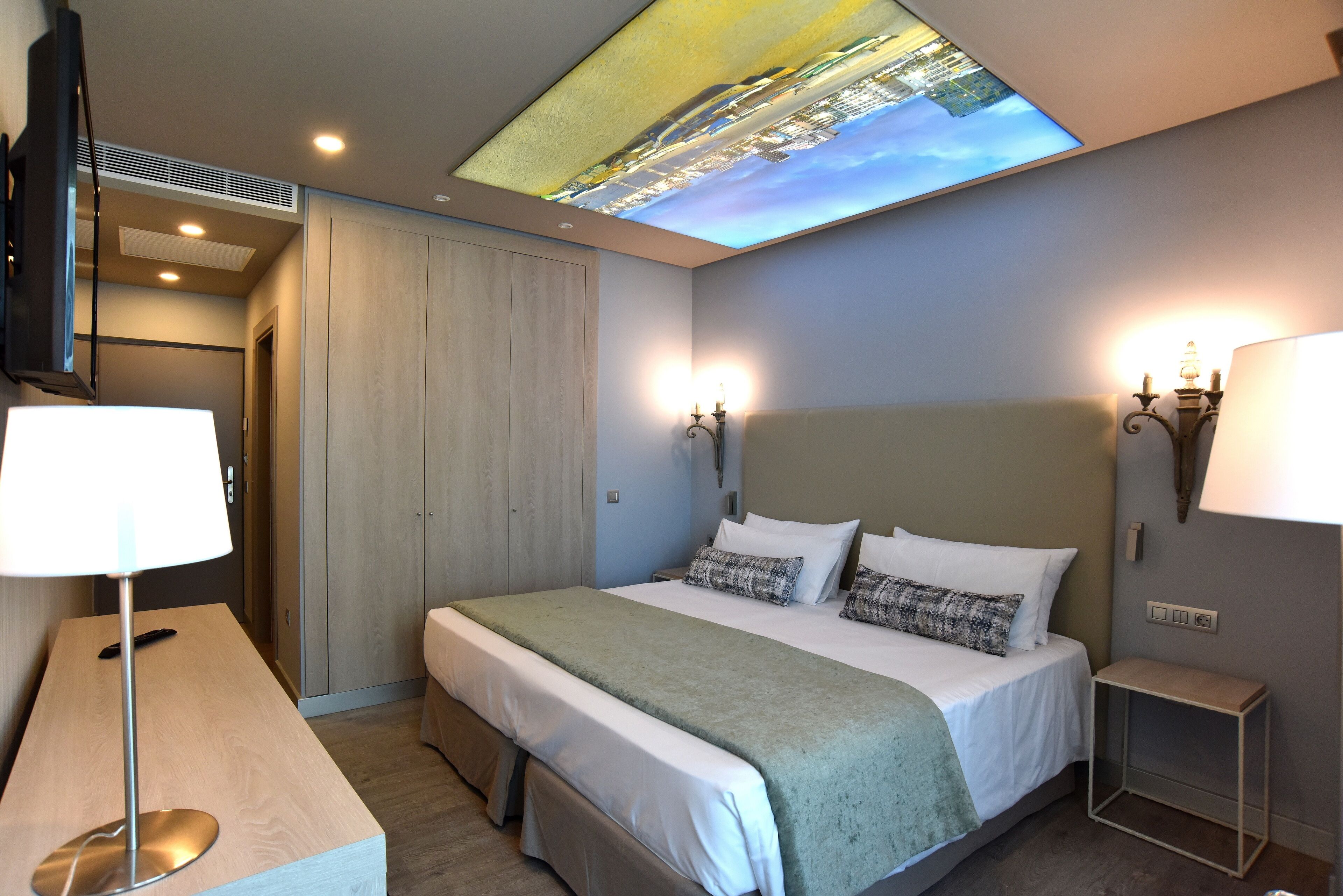 A hotel room with a bed, bedside lamps, a TV, and a ceiling projection.