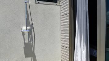 A modern outdoor shower area with a metal hose and showerhead, a small window, and a sliding glass door with a white curtain.