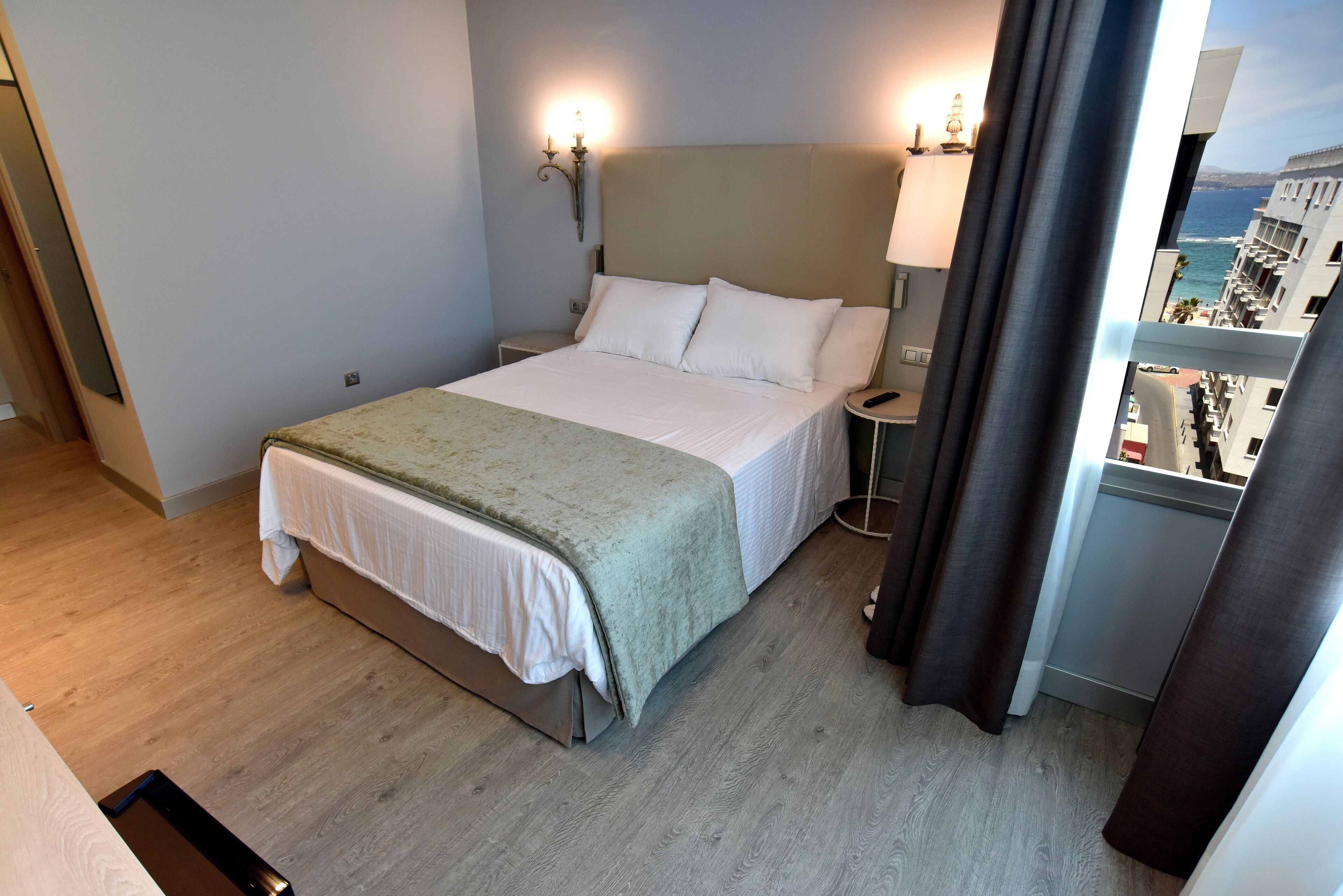 A hotel room with a bed, bedside lamps, a view of the ocean, and a balcony with curtains.