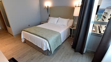 A hotel room with a bed, bedside lamps, a view of the ocean, and a balcony with curtains.