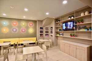 A modern restaurant with a long counter, multiple tables, and a TV mounted on the wall.