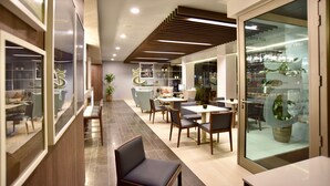 A modern interior with a long reception area, a dining section with tables and chairs, and a glass display case with items. - TC Hotel Doña Luisa (Las Palmas de Gran Canaria)