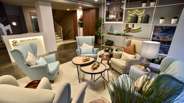 A modern hotel reception area with a reception desk, seating area with armchairs and sofas, a coffee table, and decorative plants. - TC Hotel Doña Luisa (Las Palmas de Gran Canaria)