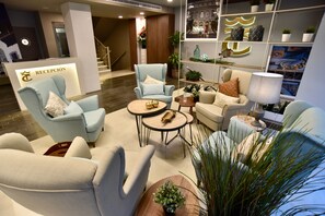 A modern hotel reception area with a reception desk, seating area with armchairs and sofas, a coffee table, and decorative plants. - TC Hotel Doña Luisa (Las Palmas de Gran Canaria)