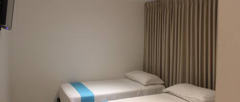 A hotel room with two single beds, a flat-screen TV mounted on the wall, and a window with beige curtains.