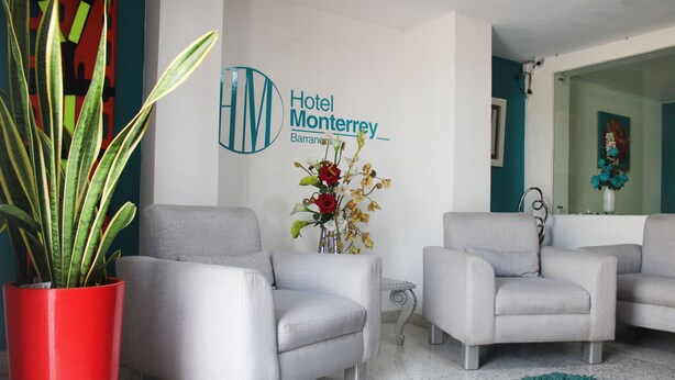 A hotel lobby with two grey armchairs, a red potted plant, a vase with flowers, and a sign for Hotel Monterrey. - Hotel Monterrey (Barranquilla)