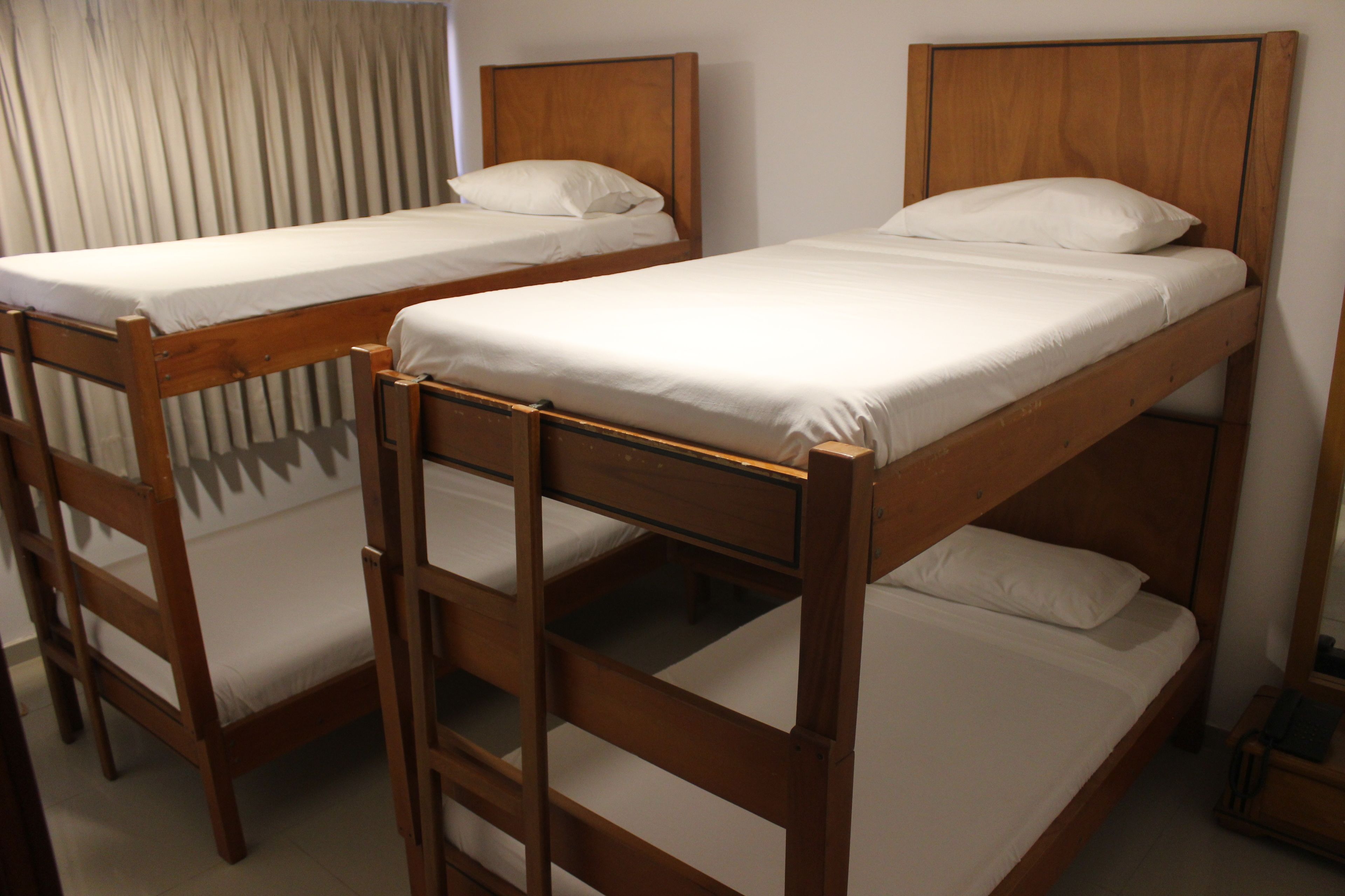 Two bunk beds with wooden frames and white bedding, arranged in a room with a curtain and a nightstand.