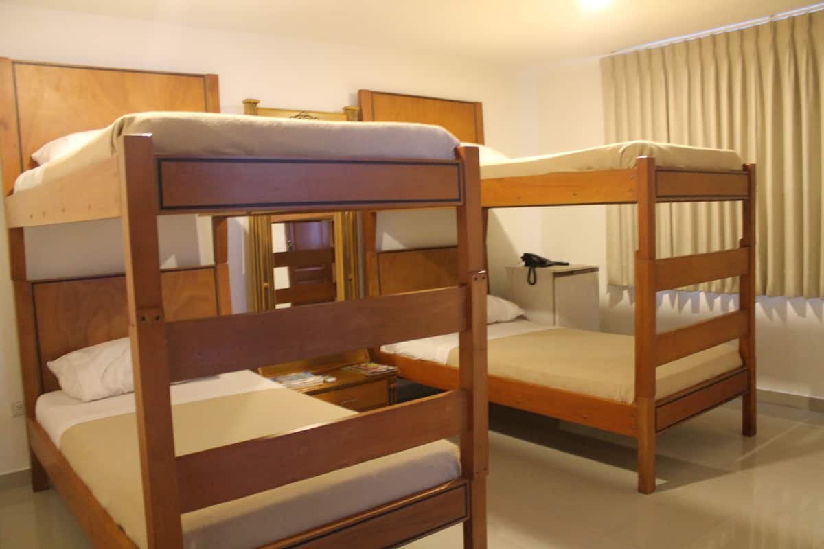 A room with two bunk beds, a bedside table with a lamp, and a window with curtains.