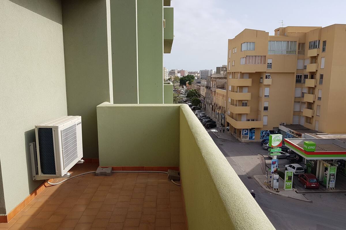 A balcony with a view of a city street, a parked car, and a gas station.