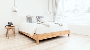 A minimalist bedroom with a wooden bed, a small bedside table with a phone, and a hanging light fixture. - Casa Legado (Bogotá)