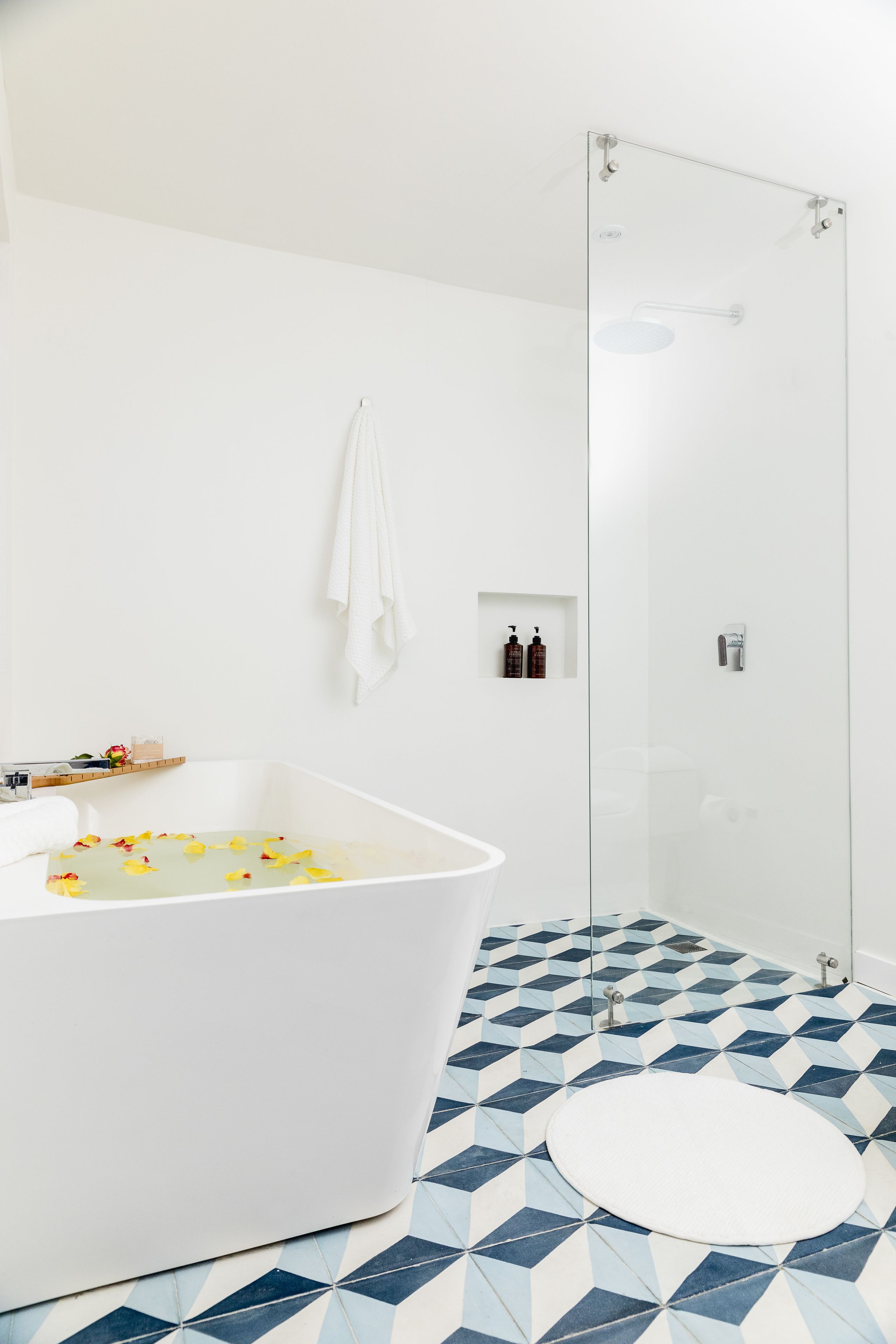 A bathroom with a freestanding bathtub, a glass shower enclosure, and a patterned floor.