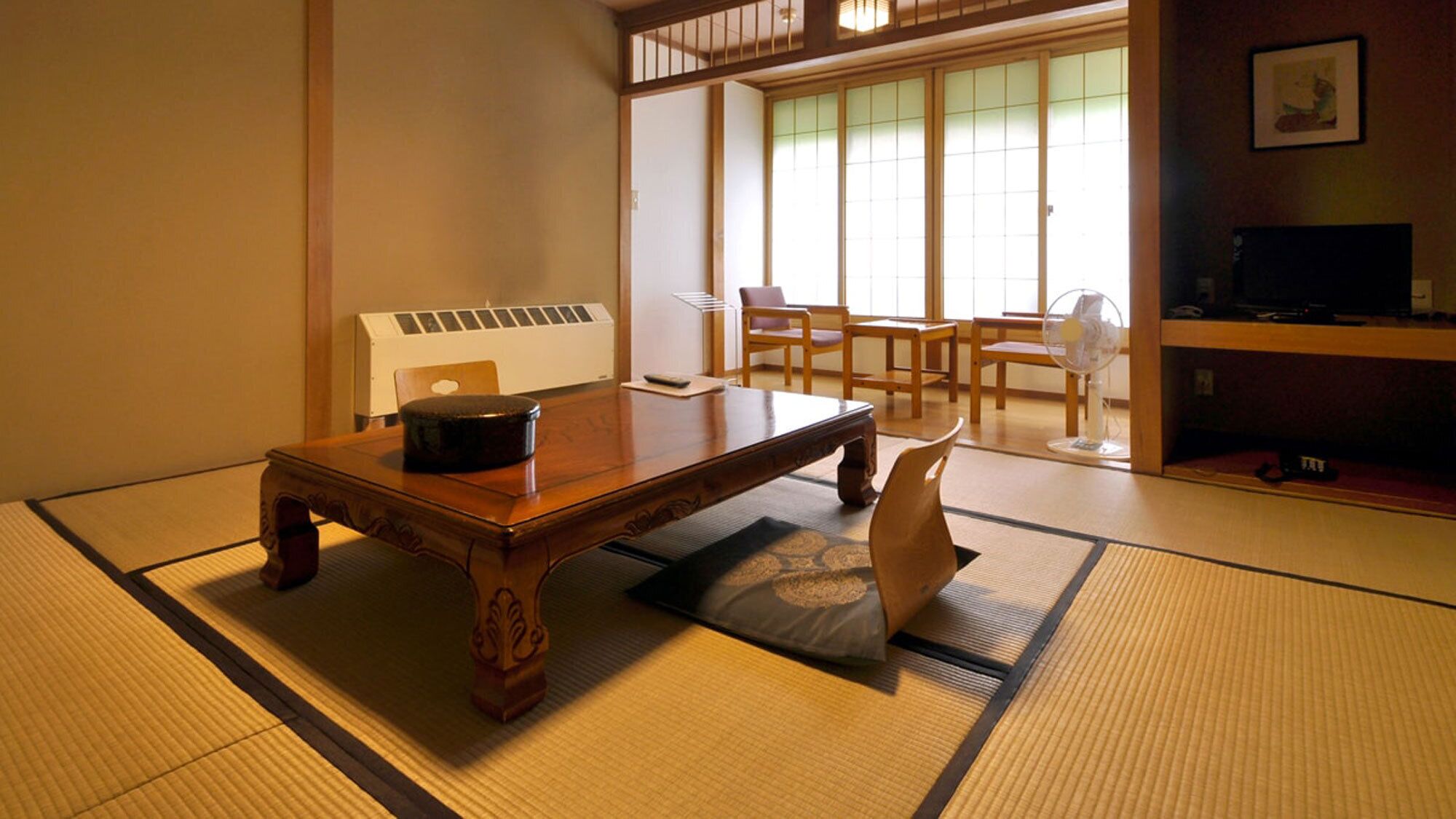 A tatami mat room with a wooden table, a black container, and a fan.