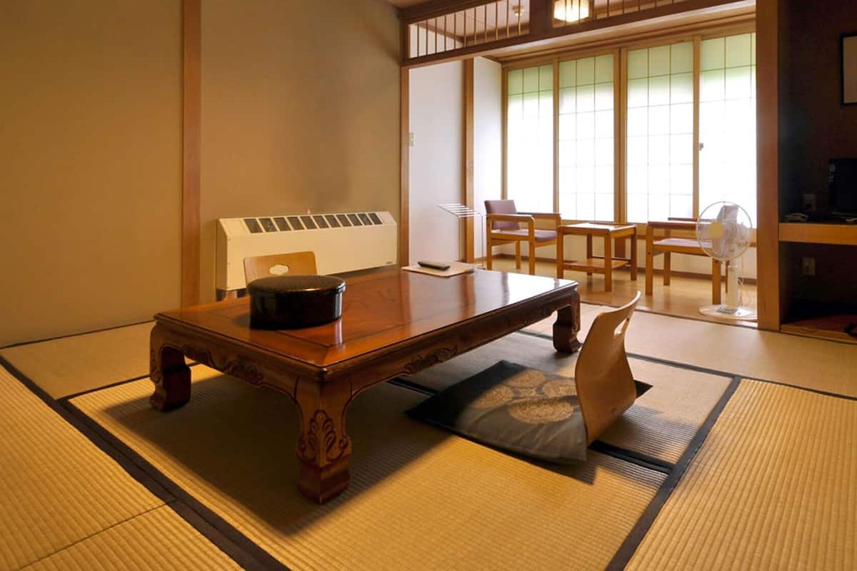 Una habitación con esteras de tatami, una mesa de madera, un recipiente negro y un abanico.