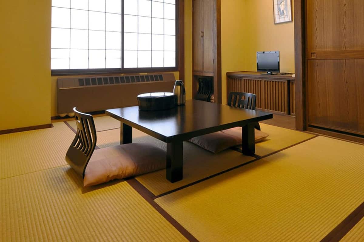 Una habitación japonesa tradicional con suelo de tatami, una mesa baja, cojines, una silla y un televisor.
