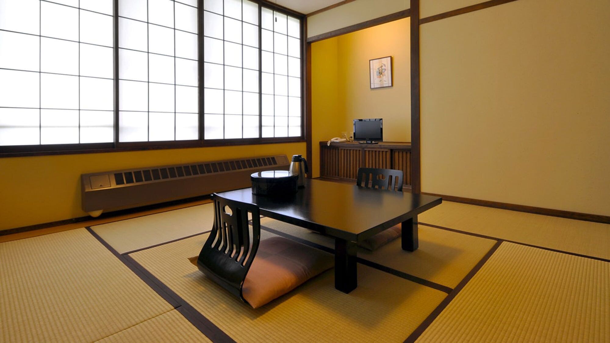 A traditional Japanese room with tatami flooring, a low table with cushions, a heater, and a television on a stand.