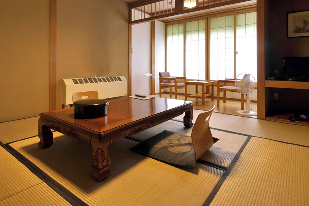 Una habitación con esterillas de tatami, una mesa de madera, un recipiente negro y un abanico.