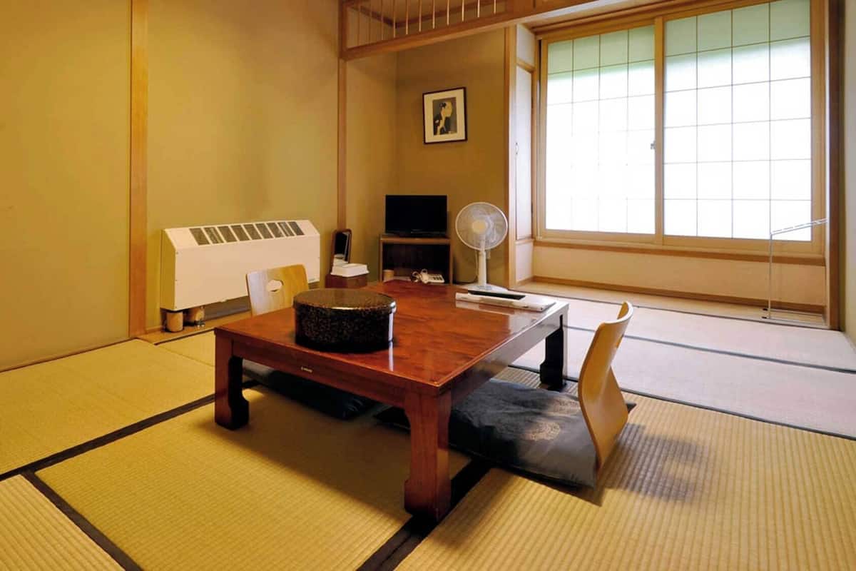 Una habitación japonesa tradicional con suelo de tatami, una mesa de madera, un calentador, un ventilador y un televisor.