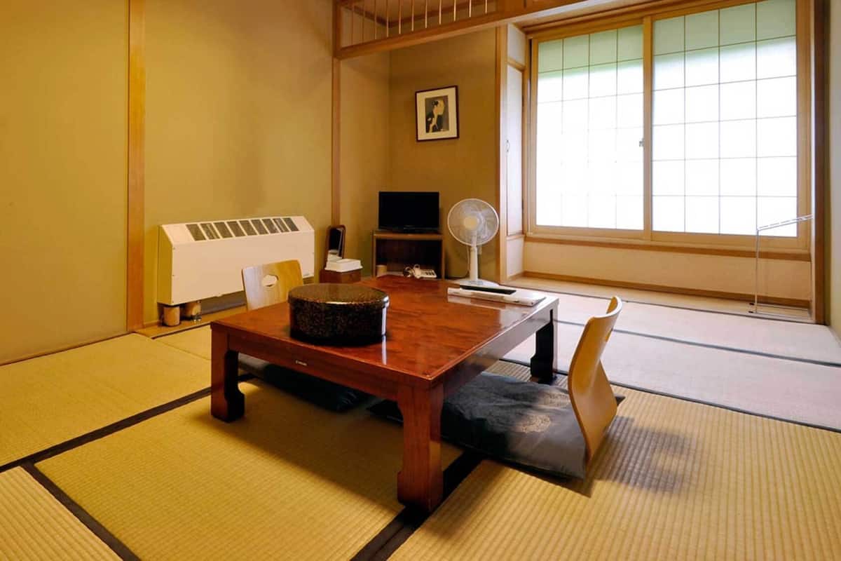 Una habitación japonesa tradicional con suelo de tatami, una mesa de madera, un abanico y un calentador.