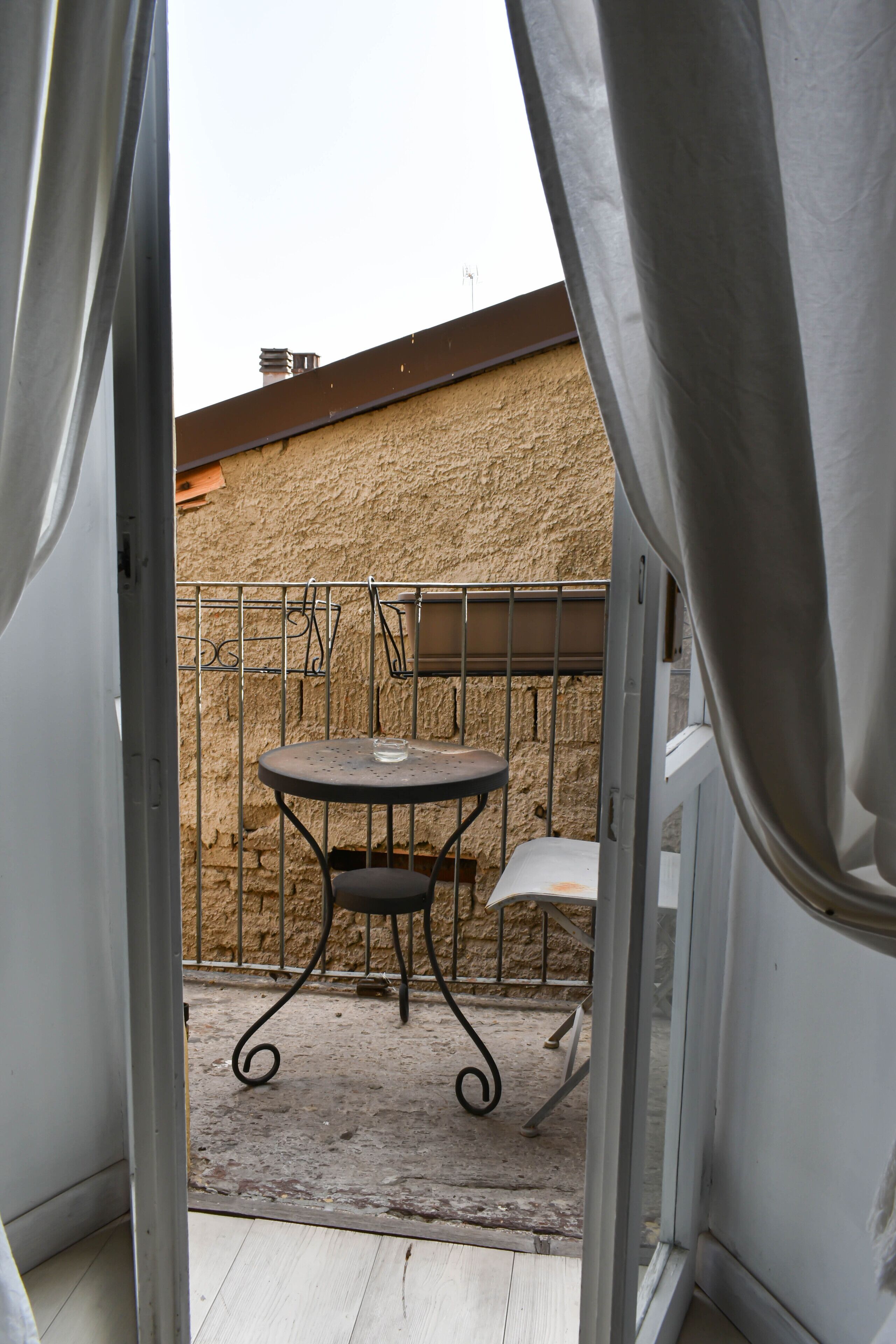 A balcony with a metal table and chair, a textured wall, and a metal railing.