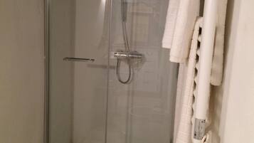 A glass-enclosed shower stall with a white toilet and a towel rack with a white towel.