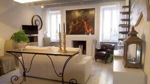 A living room with a sofa, a table with candles, a painting, a fireplace, a television, and a bookshelf.