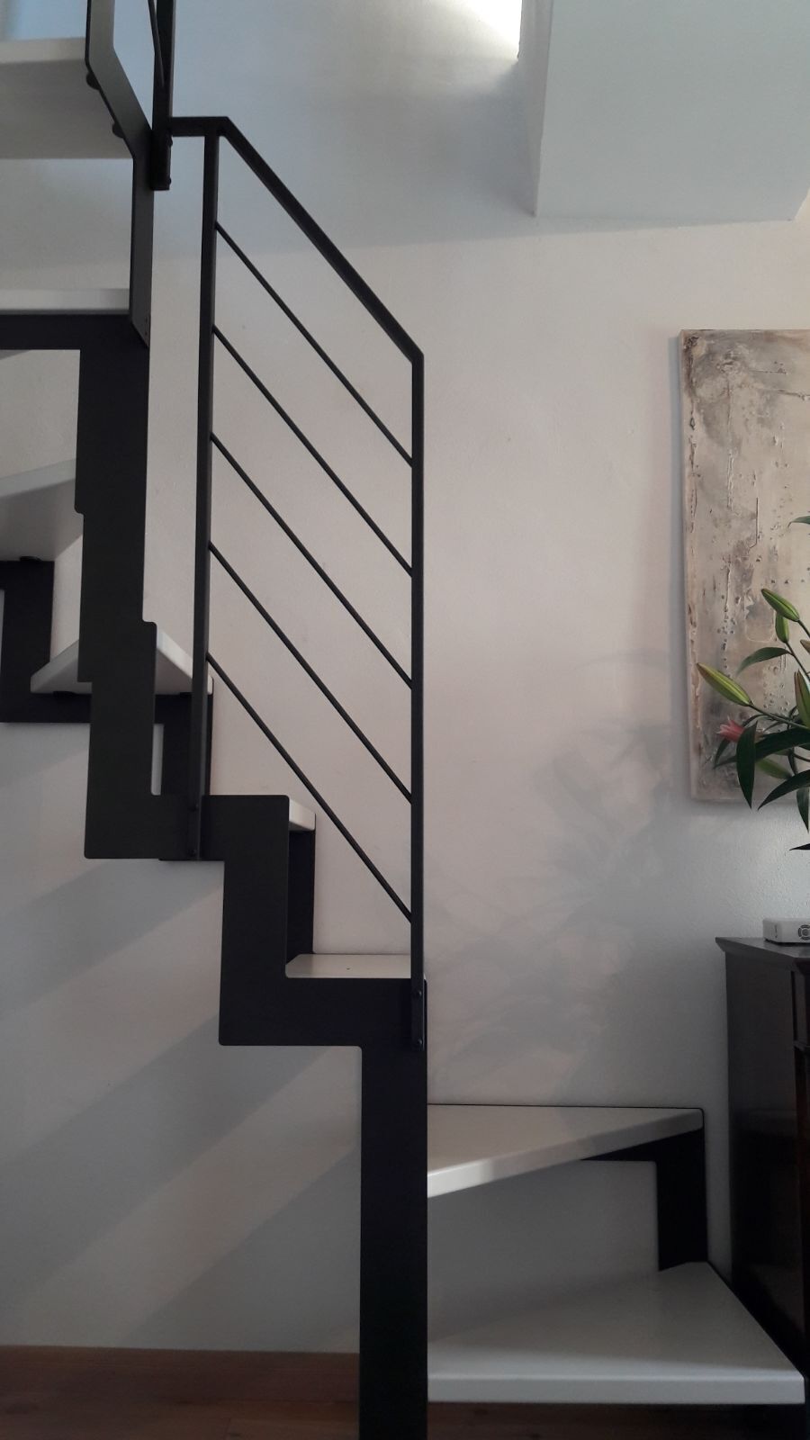 Uma escadaria moderna com guarda-corrimão preto e degraus brancos, levando a um patamar com um banco.