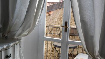Una habitación con un aparador blanco, un ventanal corredero que da a un balcón exterior con barandilla de metal y una pequeña mesa.