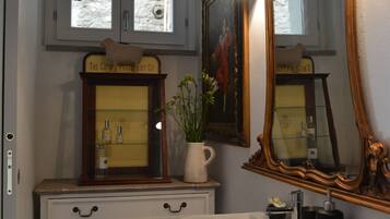 A bathroom with a white sink, a mirror, and a cabinet with drawers. There is a window above the sink and a framed picture on the wall.