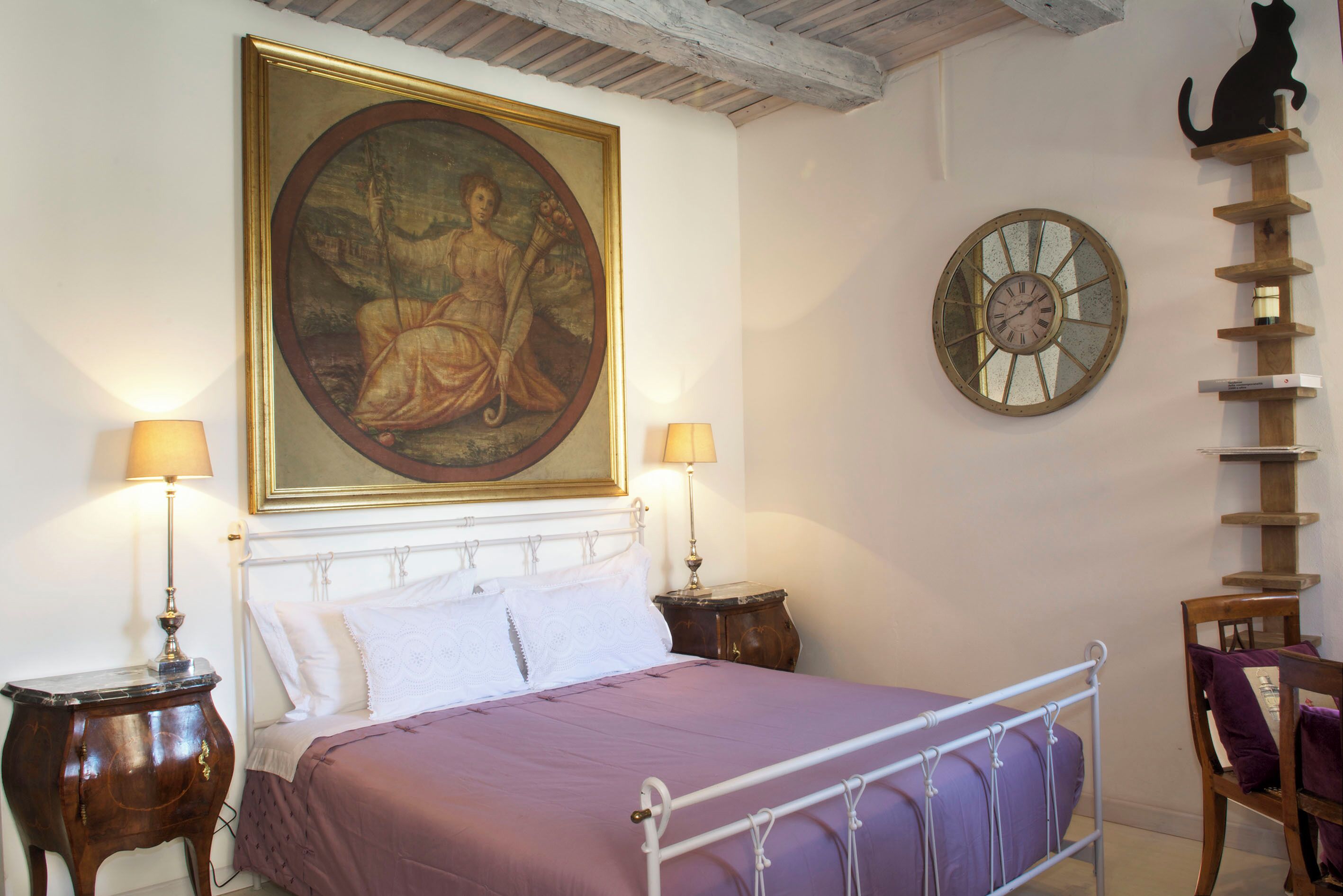 Un dormitorio con una cama, dos mesitas de noche, un reloj de pared, un estante para gatos y un cuadro enmarcado.