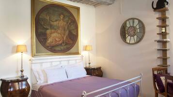 Quarto com cama, duas mesas de cabeceira, relógio de parede, prateleira para gato e um quadro emoldurado.