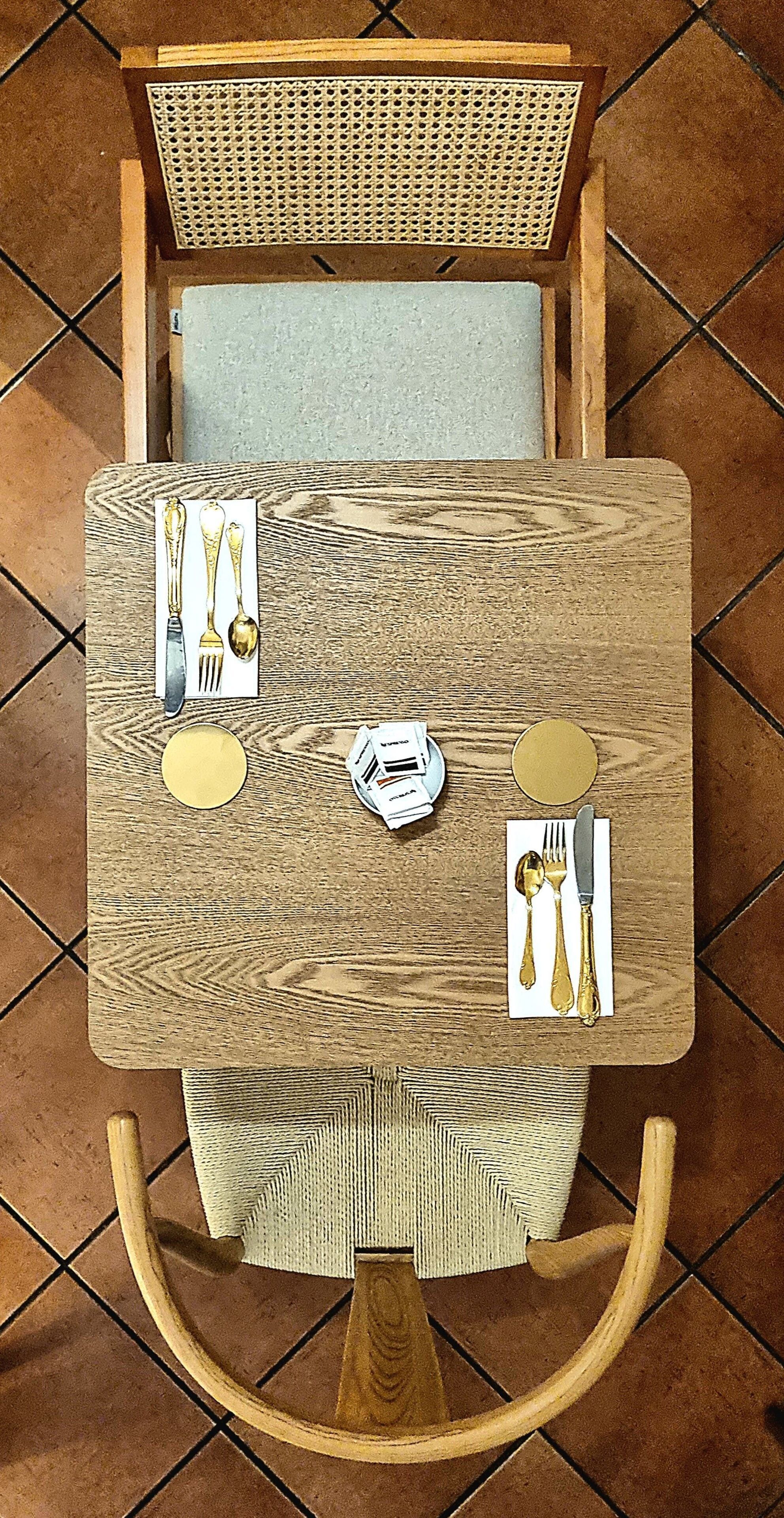 Une table carrée en bois, accompagnée d’une chaise, d’un banc et d’une tête de lit, tous trois en osier tressé.
