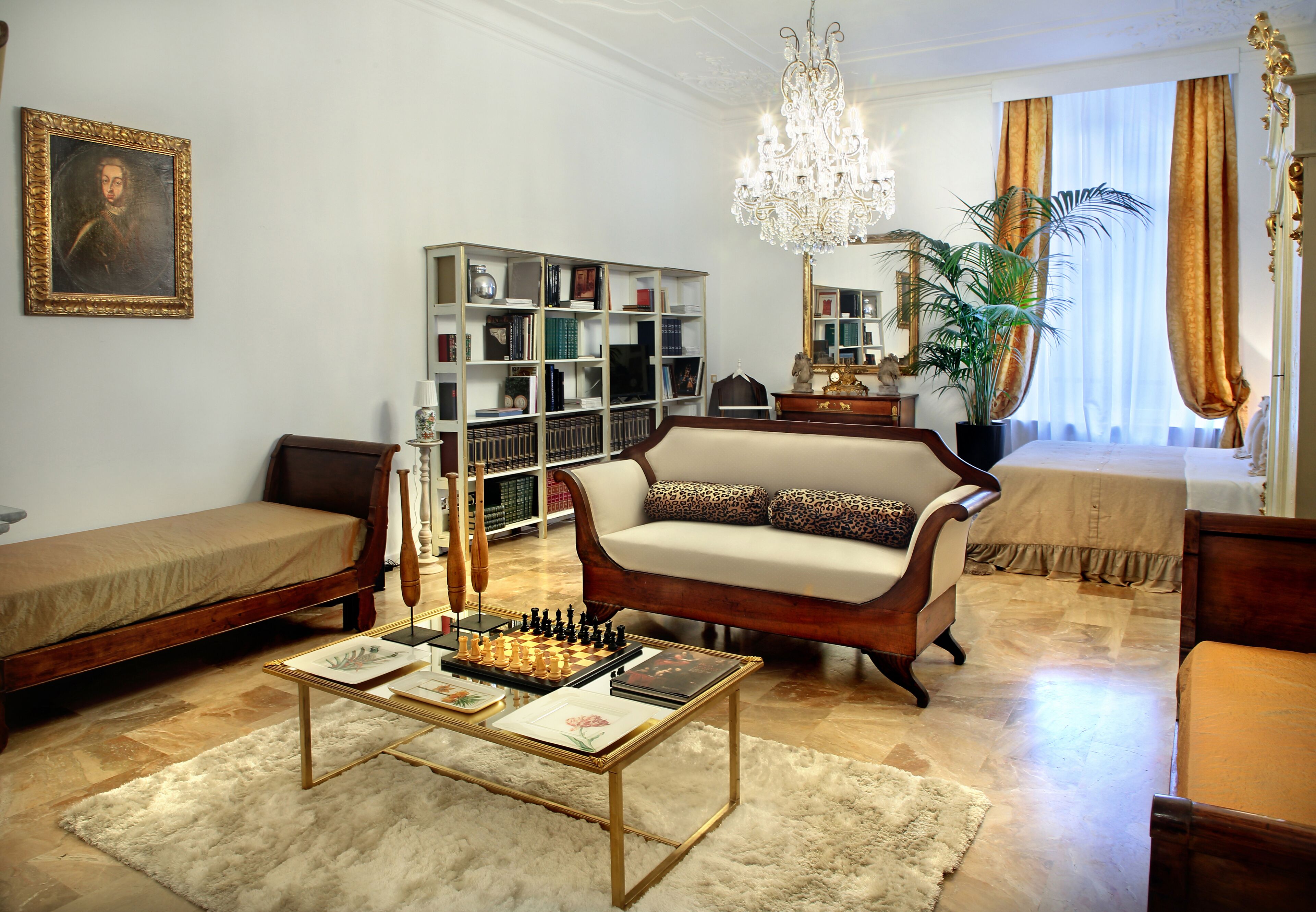Ein Wohnzimmer mit einer Couch, einem Couchtisch mit Schachfiguren, einem Bücherregal und einer Chandelieber.