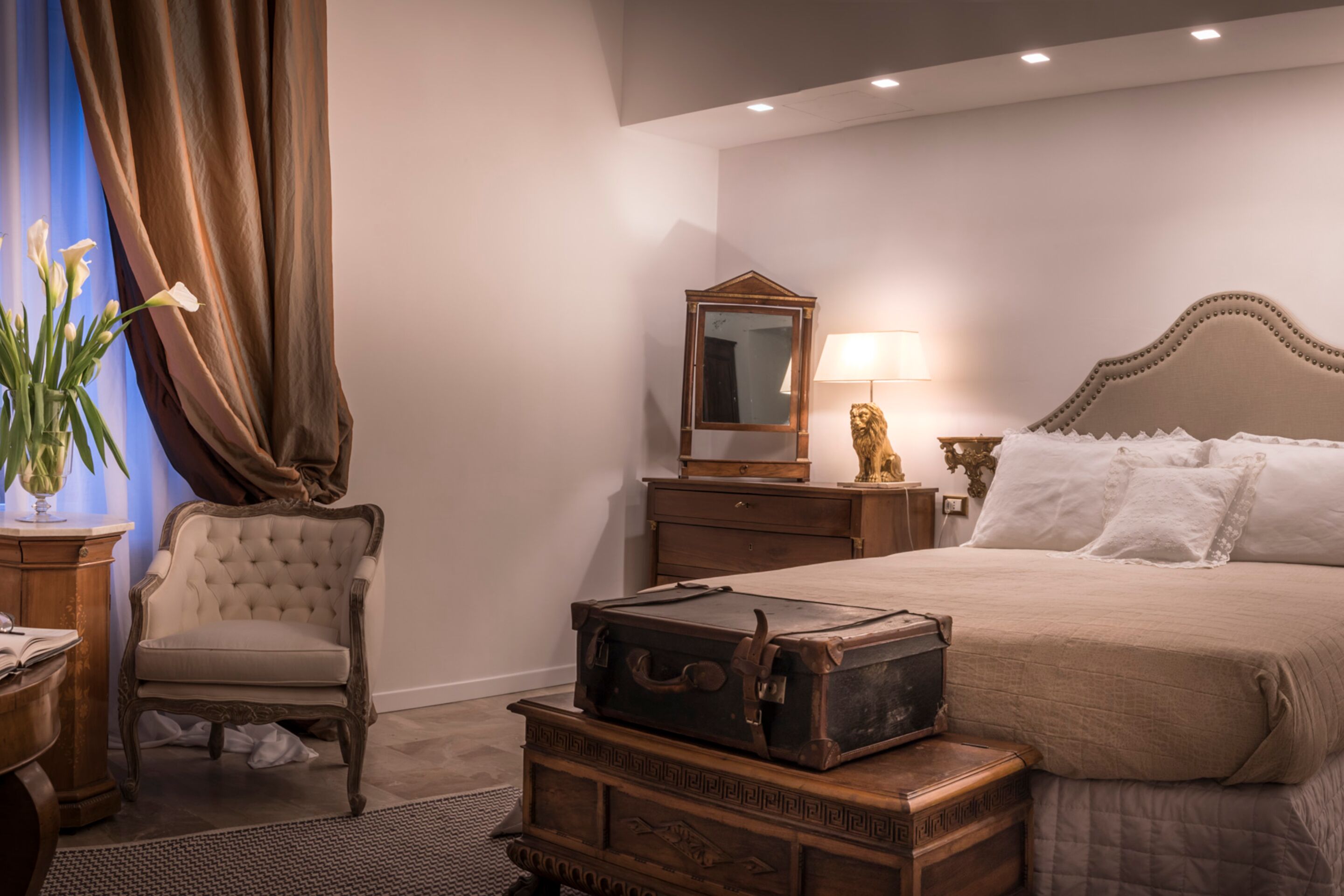 A bedroom with a large bed, a wooden dresser, a chair, and a mirror.