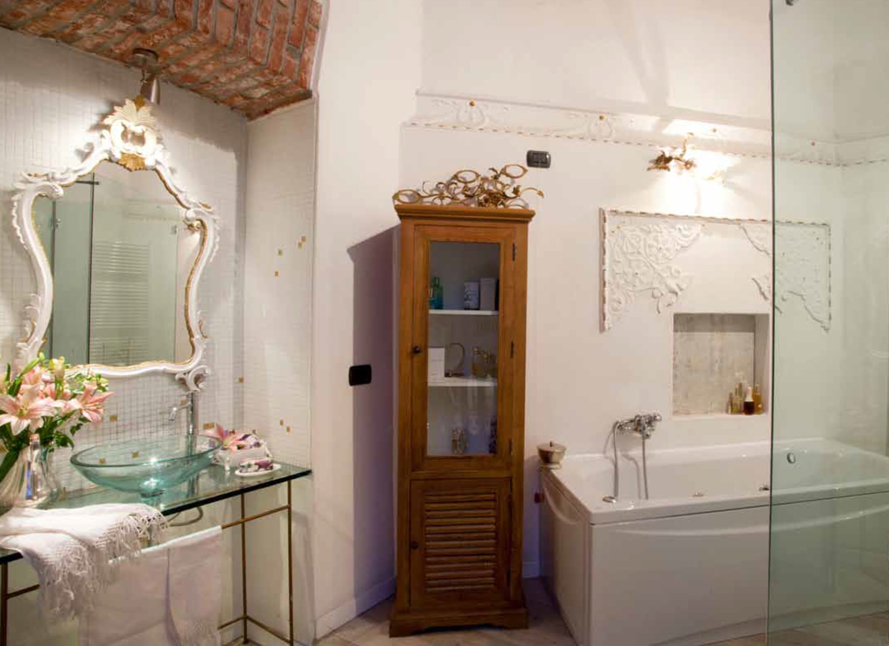 A bathroom with a glass-enclosed shower, a wooden cabinet, and a large mirror with ornate detailing.
