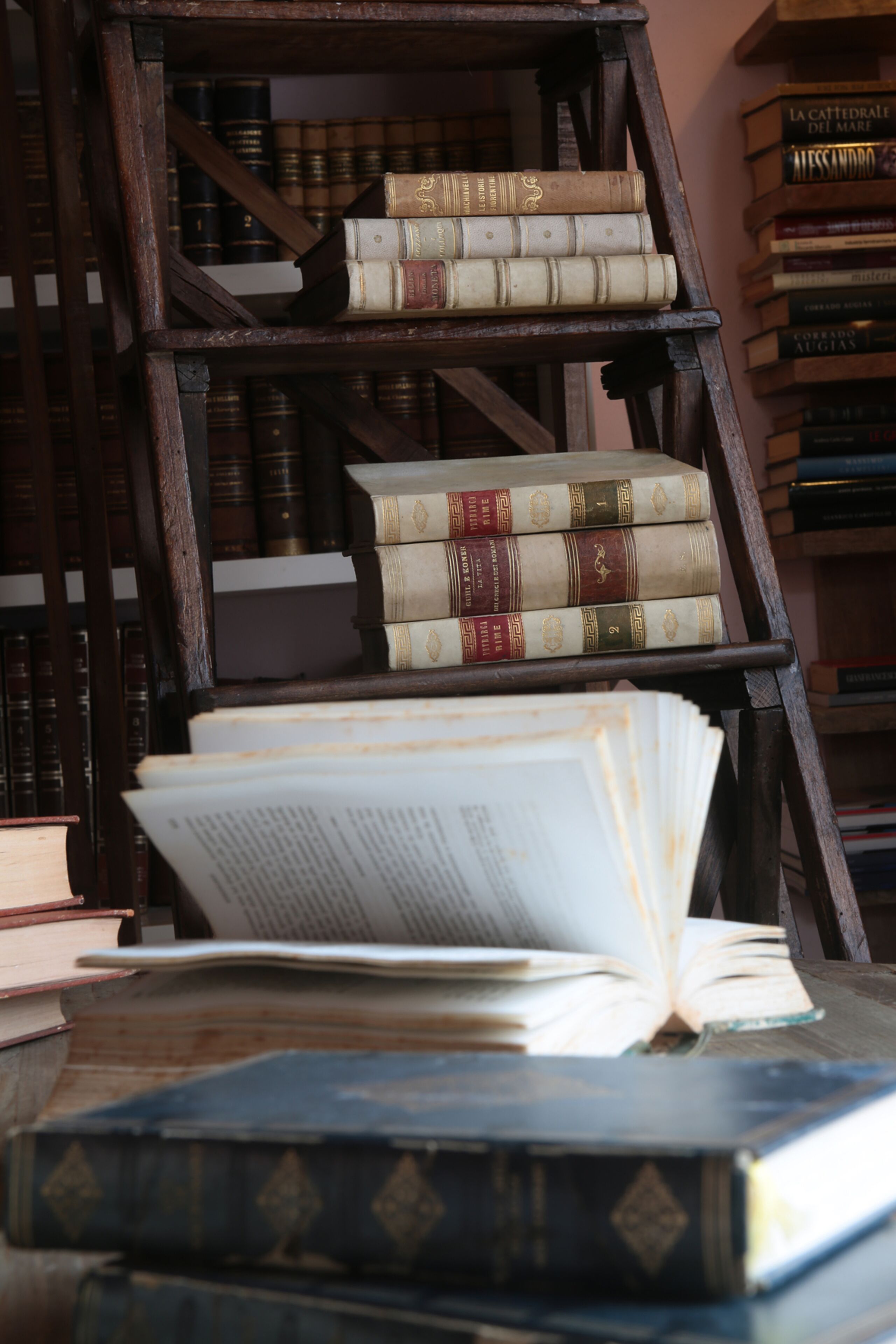A wooden bookshelf with multiple tiers of books, some open, and a few books stacked on the bottom tier.
