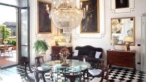 Um quarto com mesa de vidro cercada por cadeiras, um candelabro, pinturas e uma janela grande.