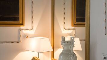 A room with a wooden side table, a white vase, a lamp, and a mirror with a gold frame.
